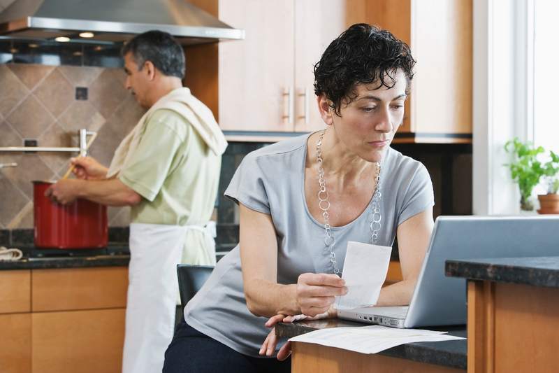 A man cooks while a woman reviews loan documents in their home's kitchen.