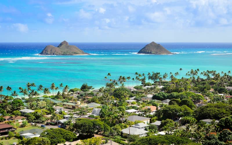 Alt text: Houses along the coast of the Mokoli'i Islands with clear, turquoise water and a bright blue sky.