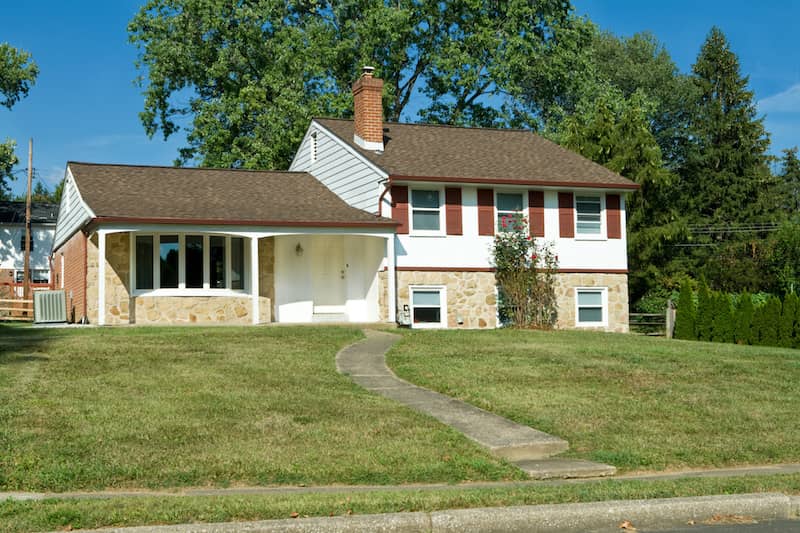 Split level home with two levels on one side and exterior made with brick, stone and siding with red shutters.