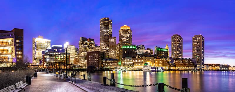 View of Boston Harbor walkway with skyline at dusk.