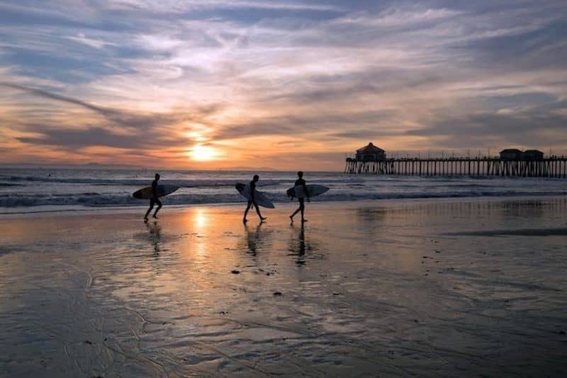 Surfers walking along beach at sunset.