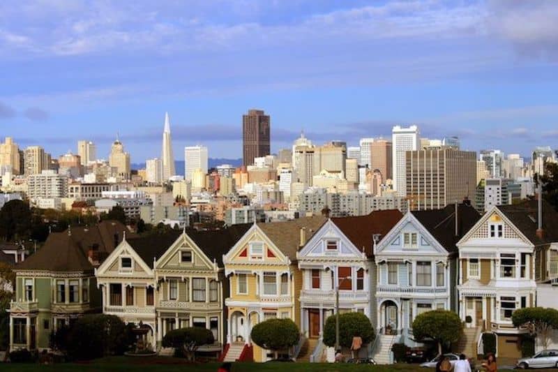 Row of Victorian homes in San Francisco with skyline in background.