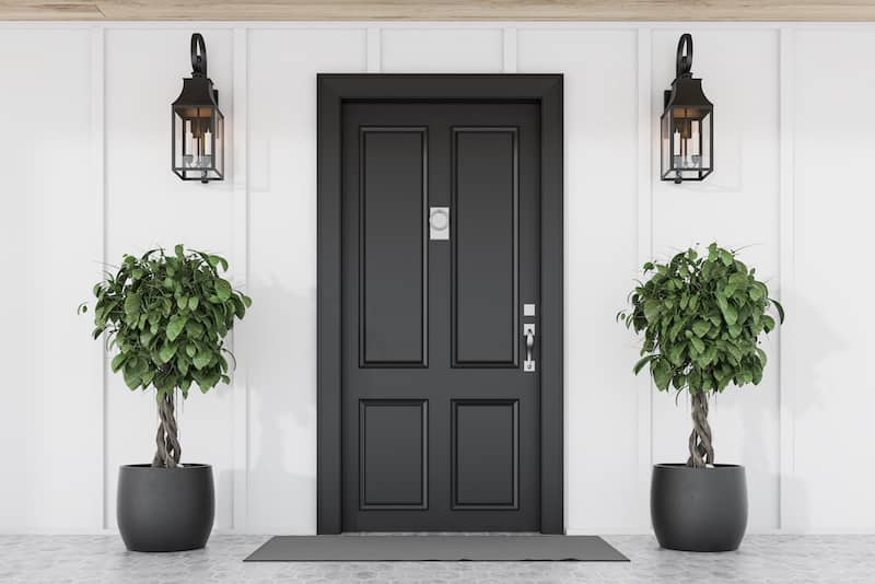 Entryway with black door, symmetrical potted plants in black pots.
