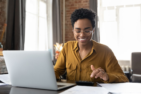 Woman smiling using calculator and laptop in home office.