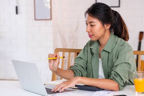 Asian woman budgeting with a calculator and her laptop at home.