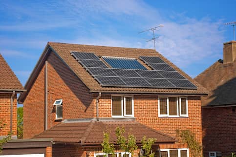 Black solar panels installed on the roof of a red brick house.