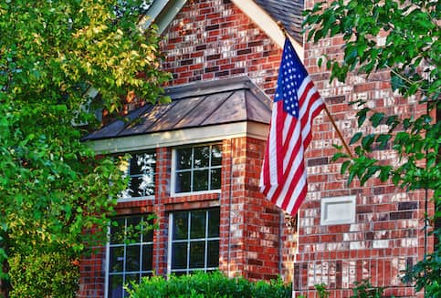 Brick two story home surrounded by trees with American flag hanging on exterior.