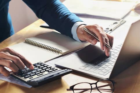 Arms of a businessman using a calculator and laptop.