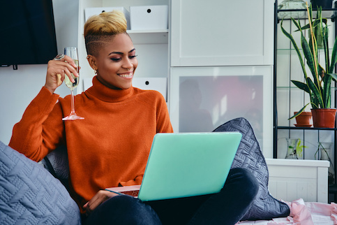 Woman on laptop on her couch with a glass of champagne.