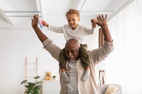 Cheerful Black Grandpa Carrying Little Grandson On Shoulders