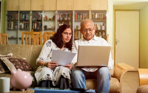 A couple sitting in their living room working on documents together on their laptop.