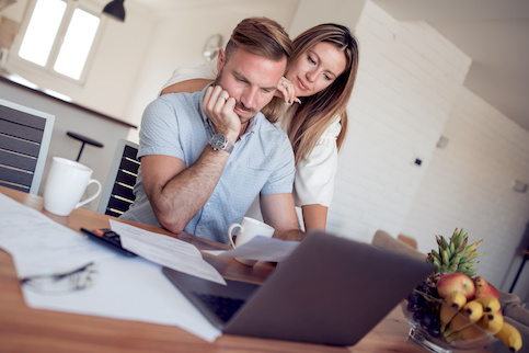 Couple reviewing finances on laptop and various paperwork spread out on kitchen table.