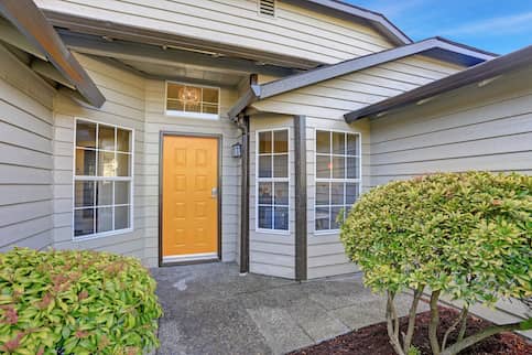 Entrance porch to a house with a bright yellow door and a bay window.