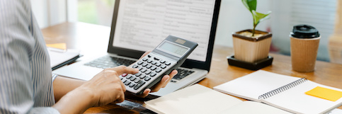 Woman calculating her mortgage rate using calculator at home office desk.