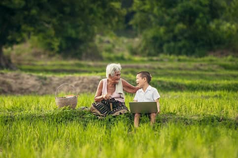 Grandmother sitting with her grandson at a farm and looking at a laptop.