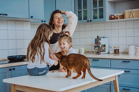 Happy young mother with two young daughters in blue and white kitchen with kitty. 