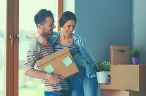 Happy young couple moving into a new home and carrying cardboard boxes.