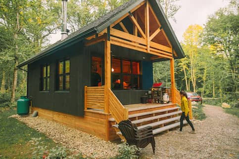 Woman walking into vacation rental forest lodge countryside cabin by the lake for holidays in the wilderness. 