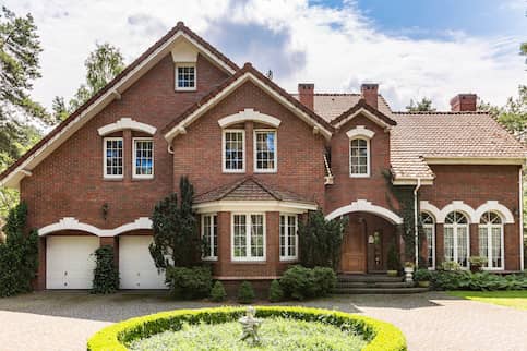 Classic English style brick home with green gardens and circle driveway.