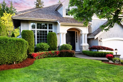Large white home's exterior with large yard and many hedges.