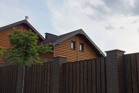 The loft of a private wooden house with windows seen from behind a brick fence.