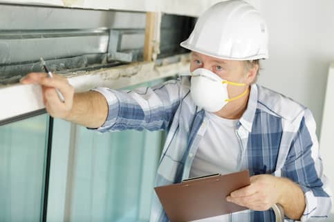 Man inspecting a property while wearing a white face mask and helmet.