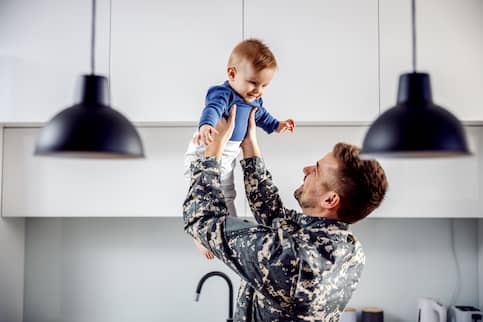 Man in military uniform holds toddler son.