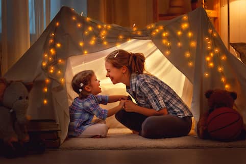 Mother and daughter play in a sheet tent in living room.