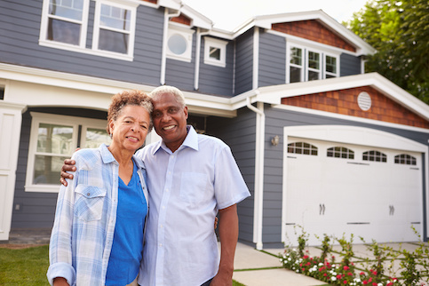 Older couple embracing happily in front of new home.