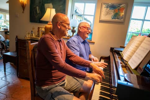 Senior gay couple playing a piano together.