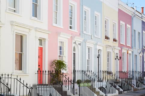 Pastel row of historic townhomes with black wrought iron fences in front.