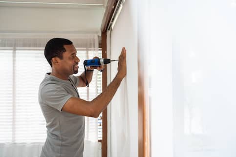 A person using drill on wall in home.