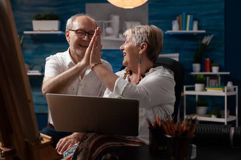 Senior couple at home using laptop and high-fiving each other.
