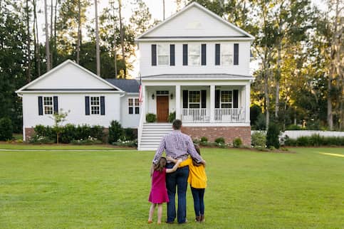 Single father stands in front of hew home with daughters.