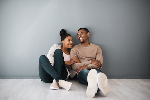 Smiling man and woman sitting, cuddling on floor of new home.