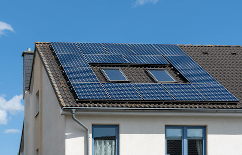 Solar panels on black tiled roof of white stucco home against backdrop of blue sky.