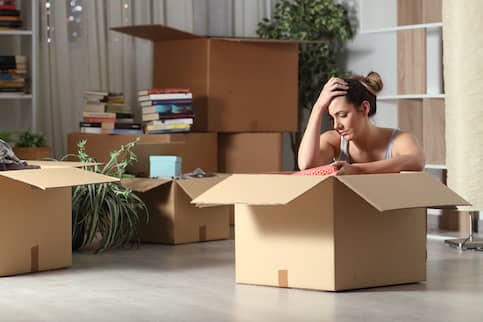 Dejected looking woman packing a cardboard box while sitting on the floor.
