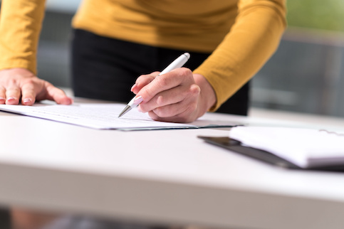 Woman in yellow shirt signing paperwork.