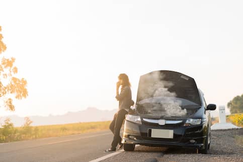 A woman leaning against her broken down car on the side of the road.