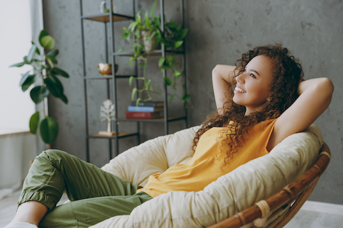 Young woman happily relaxing in comfy chair in living room surrounded by plants.