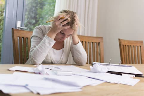 A woman looking stressed while looking at a lot of paperwork.