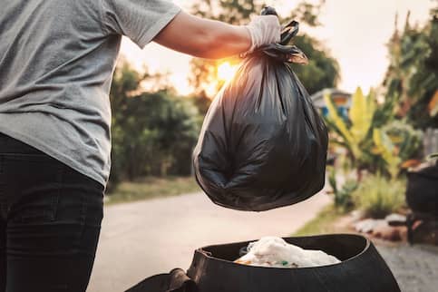 Woman throwing away bag of trash.