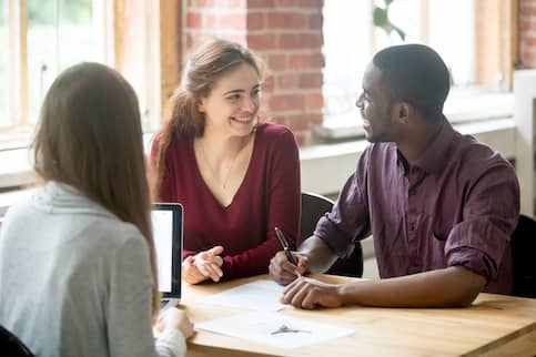 Interracial couple signing mortgage documents with real estate agent.