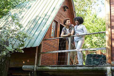 Young couple enjoying hanging out on upper deck of treehouse style cabin in the woods.