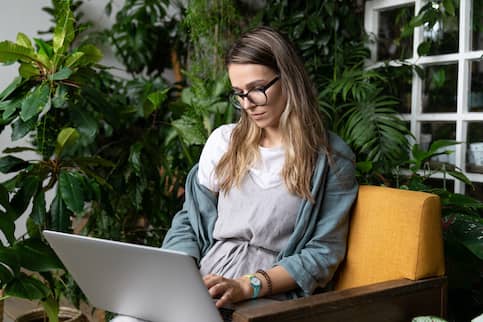 Young woman on laptop in all seasons room surrounded by plants.