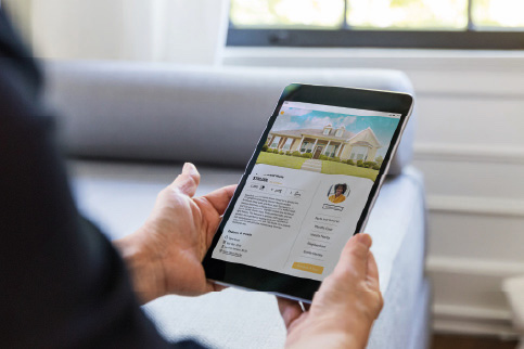 Person holding a tablet in both hands showing a house listing.