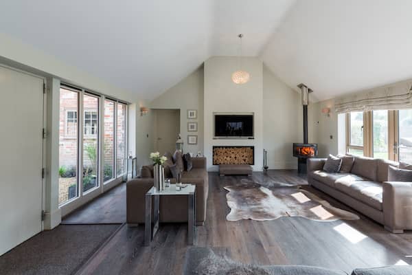 Sleek interior of contemporary barndominium living room featuring wood burning fireplace and plenty of natural light.