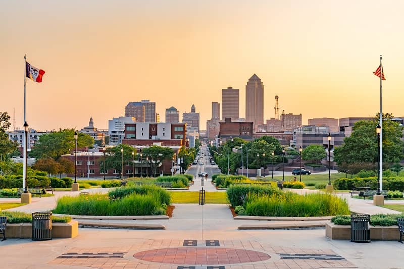 View of Des Moines skyline at sunset from park with two flags and landscaping.
