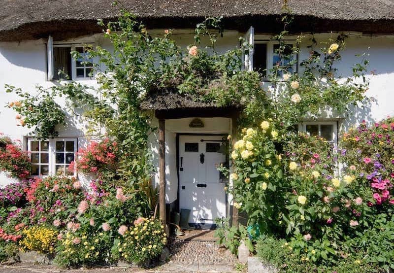 Entryway of English cottage with lush floral garden surrounding doorway and path.