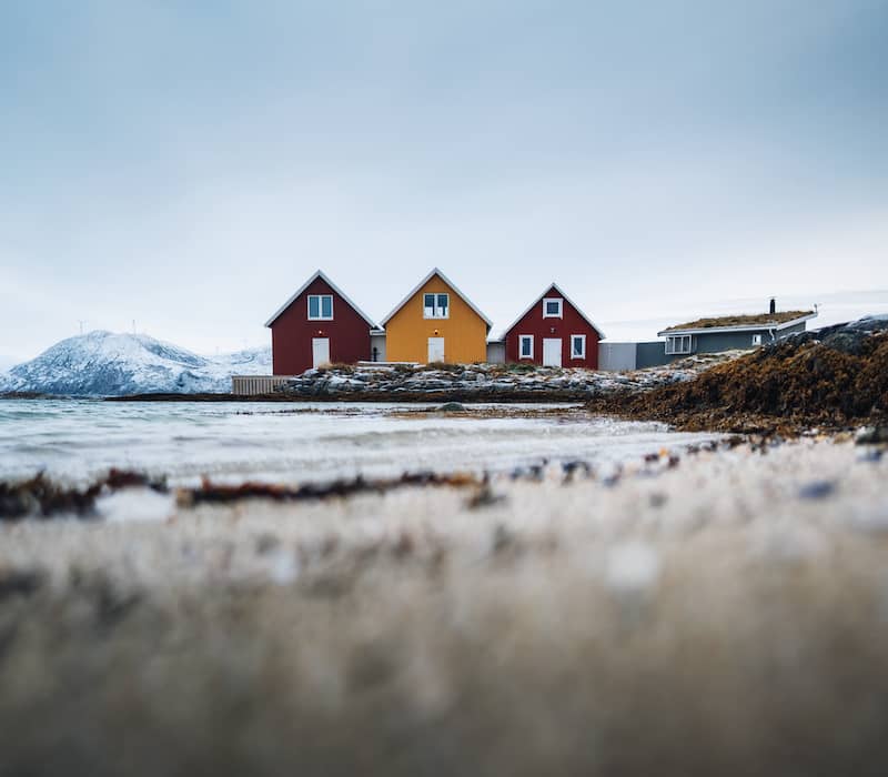 Row of three red and orange Nordic style cottages in a remote wintry landscape.